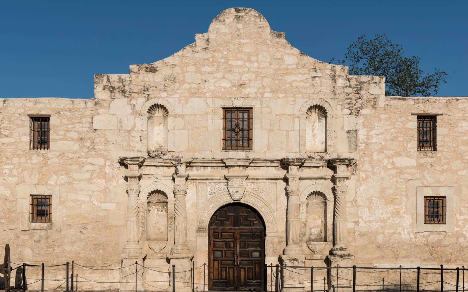 Limestone facade of the Alamo mission church in San Antonio, Texas, under a clear blue sky
