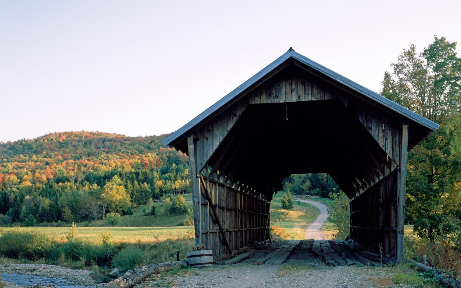 Wooden covered bridge with autumn foliage on the hillside behind it in rural Vermont